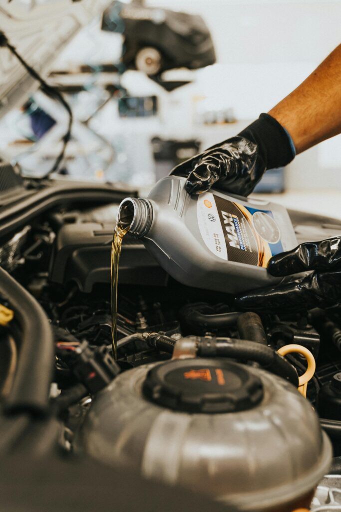 pexels photo 13065694 13065694 A close-up of a mechanic in gloves pouring engine oil into a car engine, showcasing automotive maintenance.