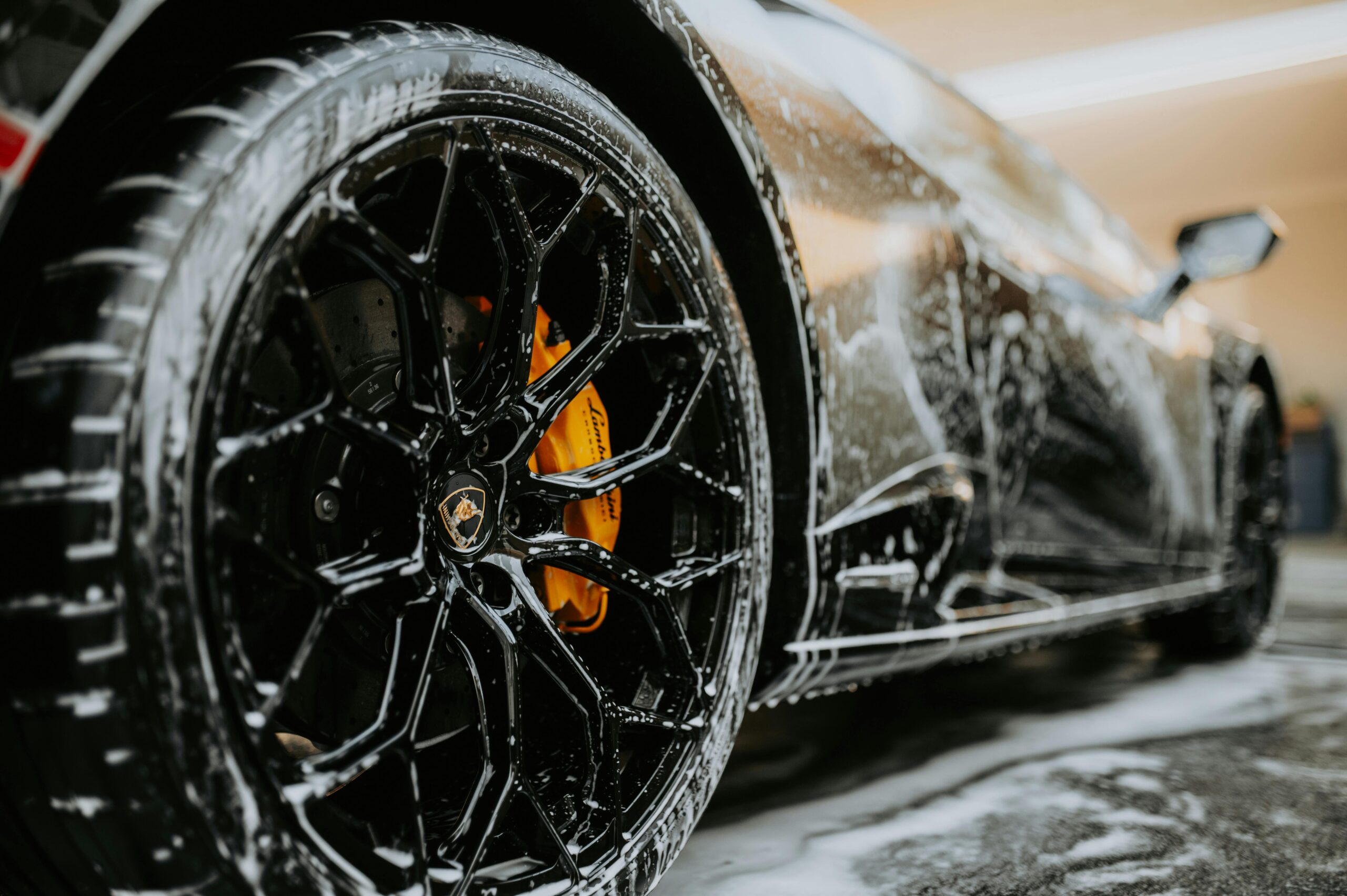 menu-01 Detailed close-up of a luxury car wheel covered in soap suds during a professional car wash.